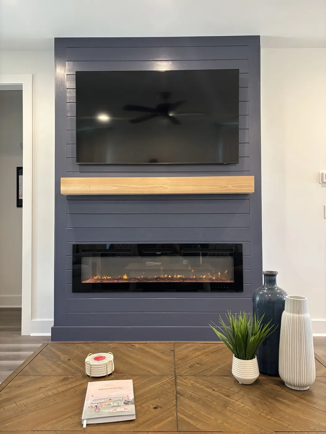 Completed dark blue fireplace feature wall with television, wood mantel, and linear electric fireplace